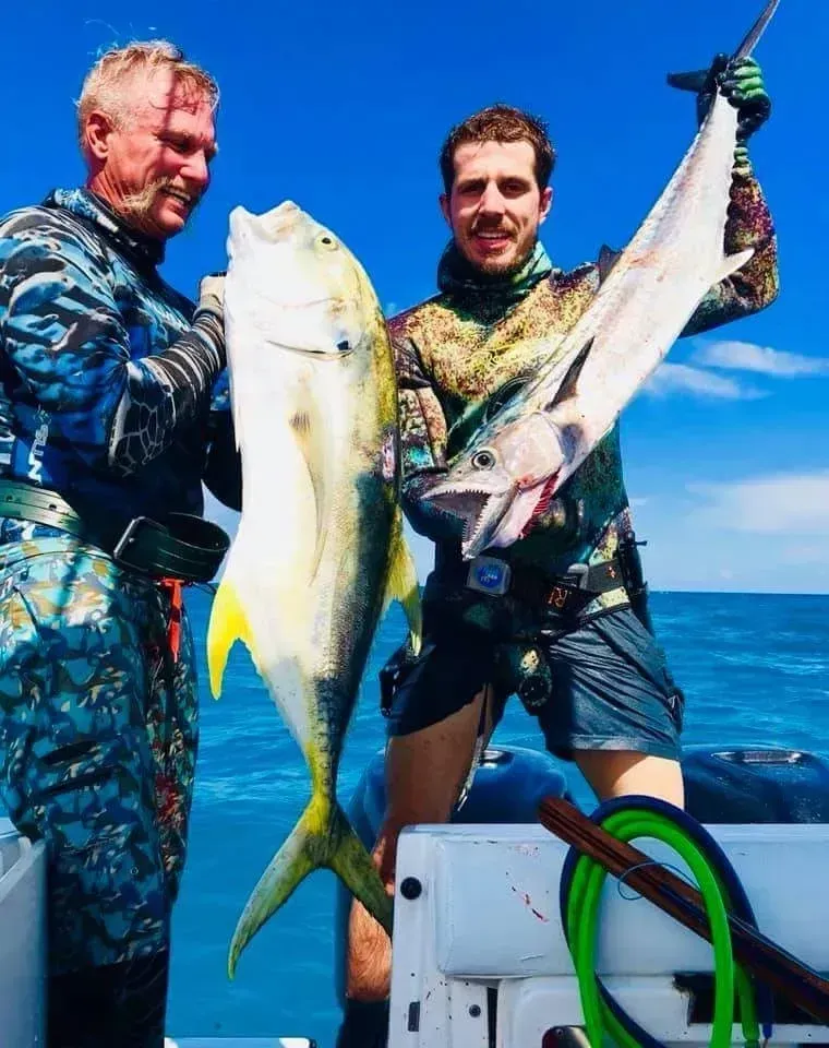 Two men are holding fish on a boat in the ocean