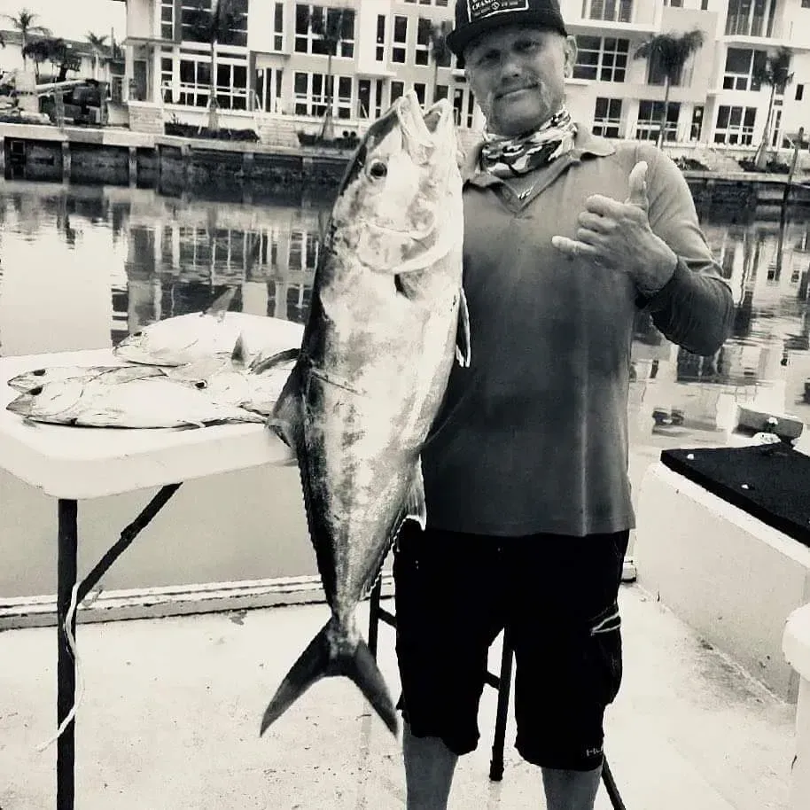 A man is holding a large fish in front of a table with fish on it