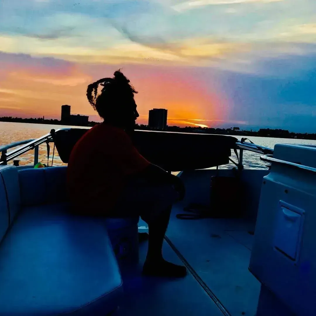 A man is sitting on a boat looking at the sunset