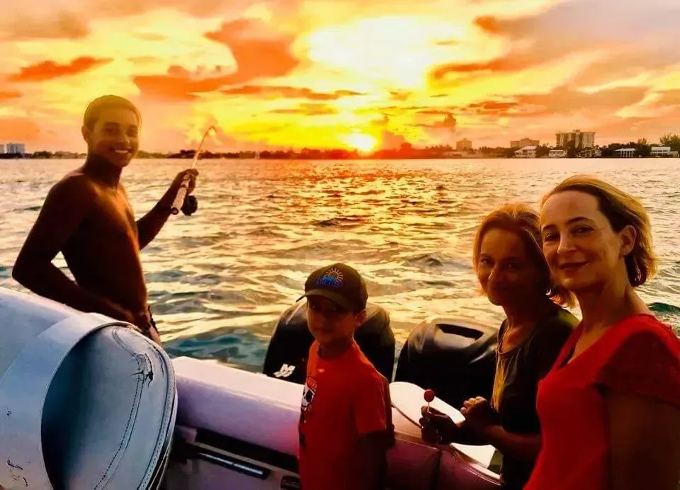 A group of people are standing on a boat in the water at sunset.