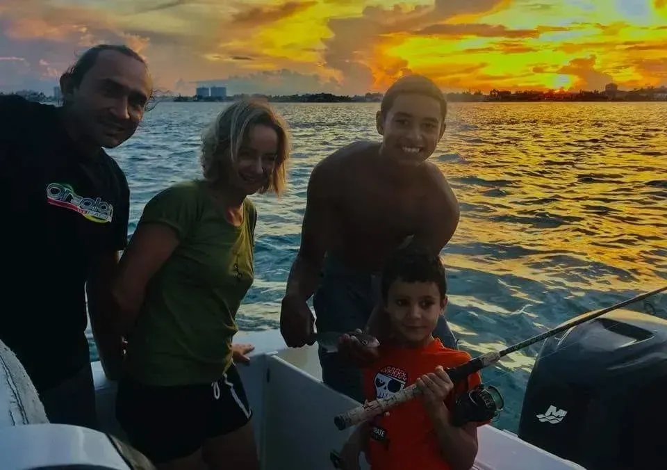 A group of people are standing on a boat in the water at sunset.