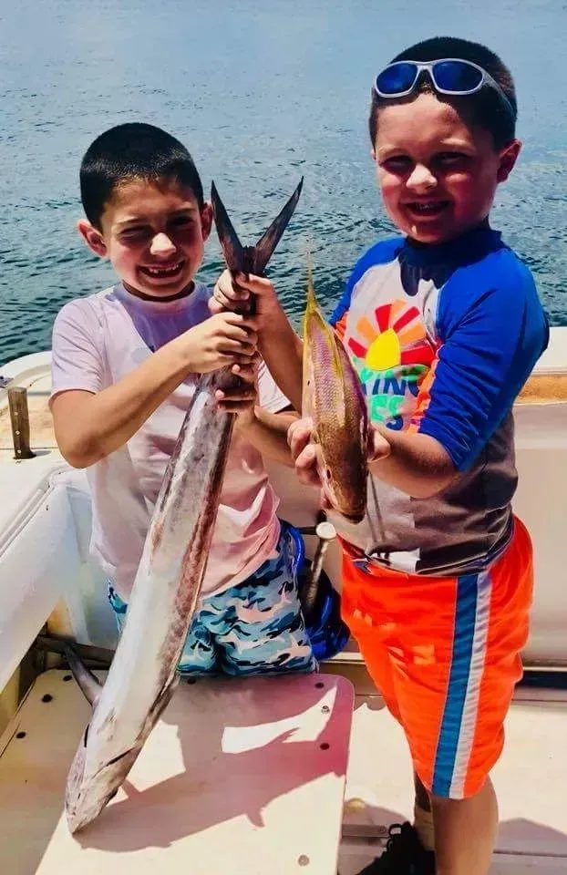 Two young boys are holding a large fish on a boat.