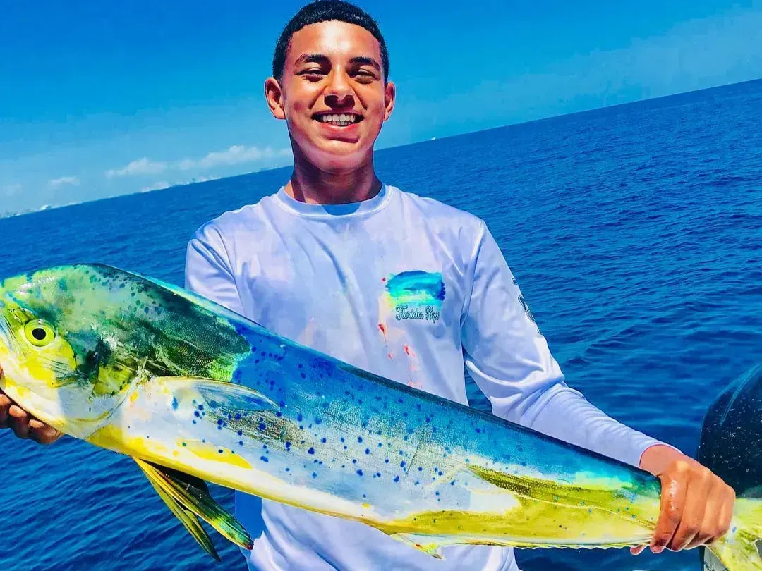 A young man is holding a large fish in the ocean.