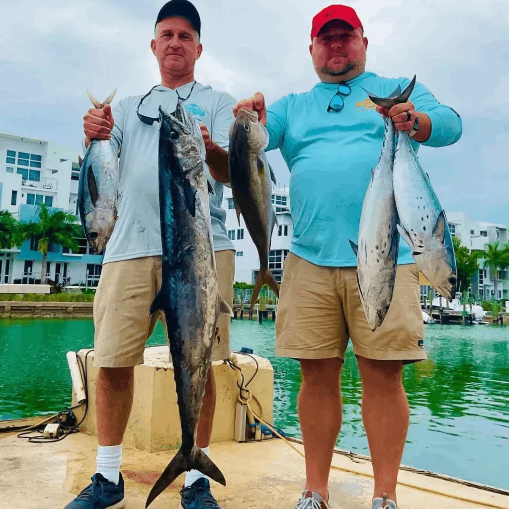 Two men standing on a dock holding fish in their hands
