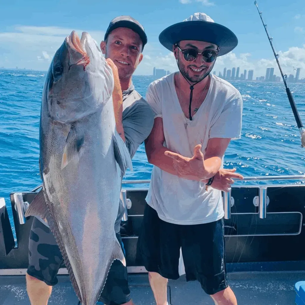 Two men are standing on a boat holding a large fish.