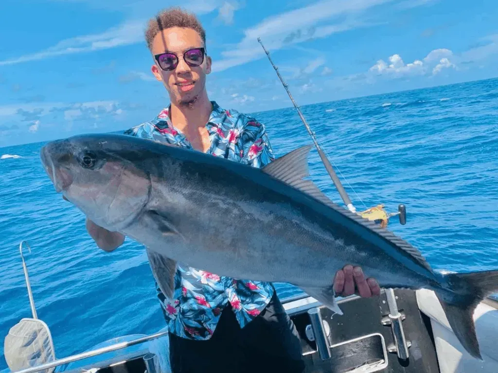 A man is holding a large fish on a boat in the ocean.