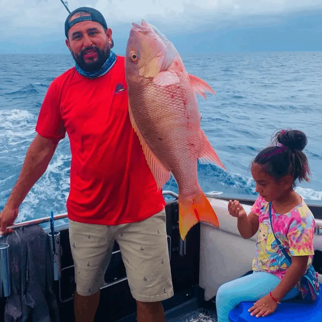 A man in a red shirt is holding a large fish