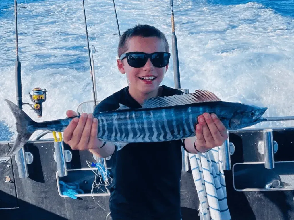 A young boy is holding a large fish on a boat.