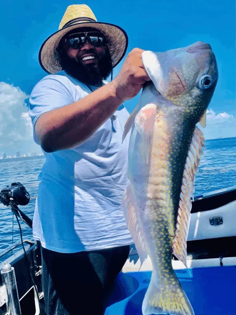 A man in a straw hat is holding a large fish on a boat.