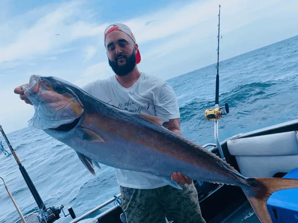 A man is holding a large fish on a boat in the ocean.