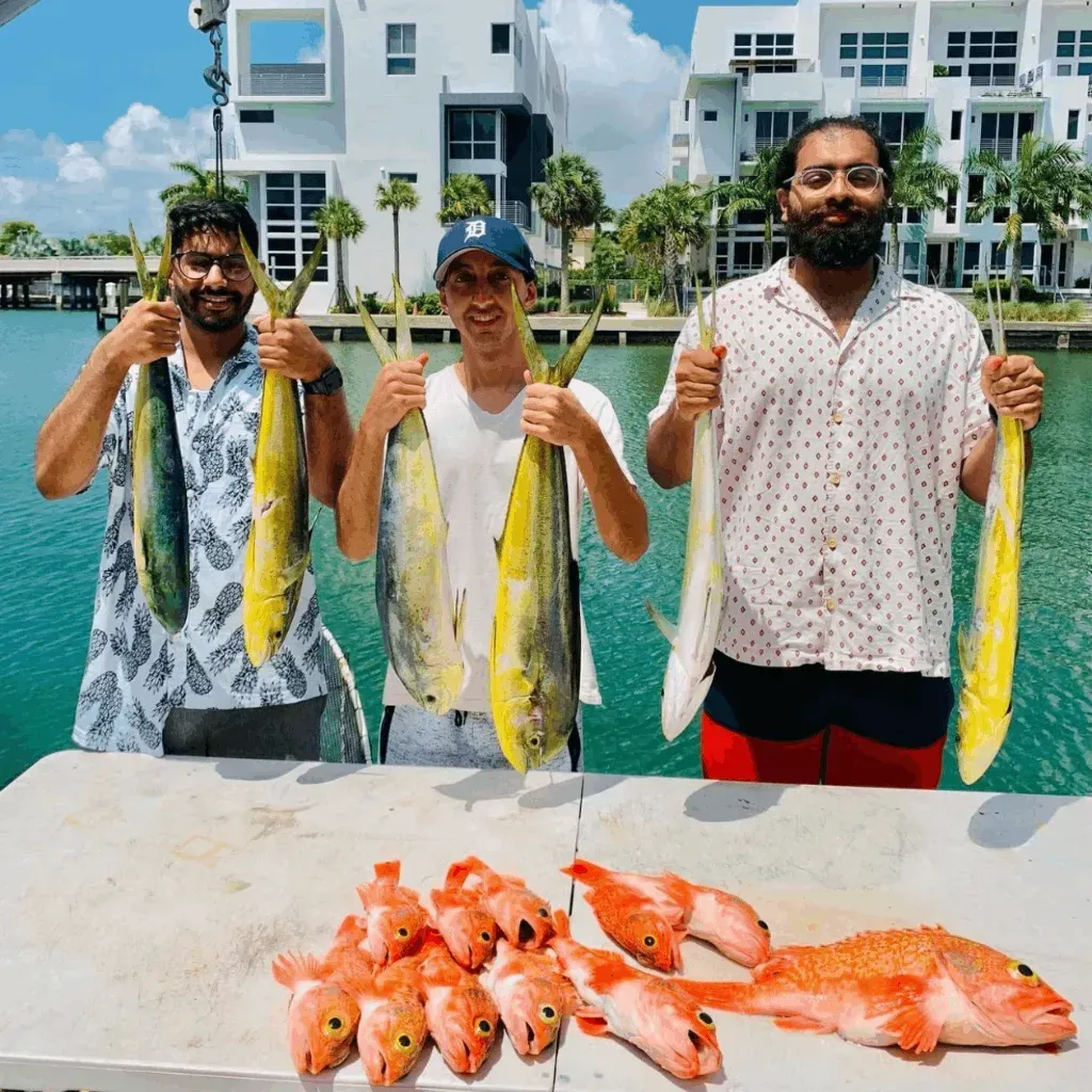Three men are holding fish in front of a table full of fish.