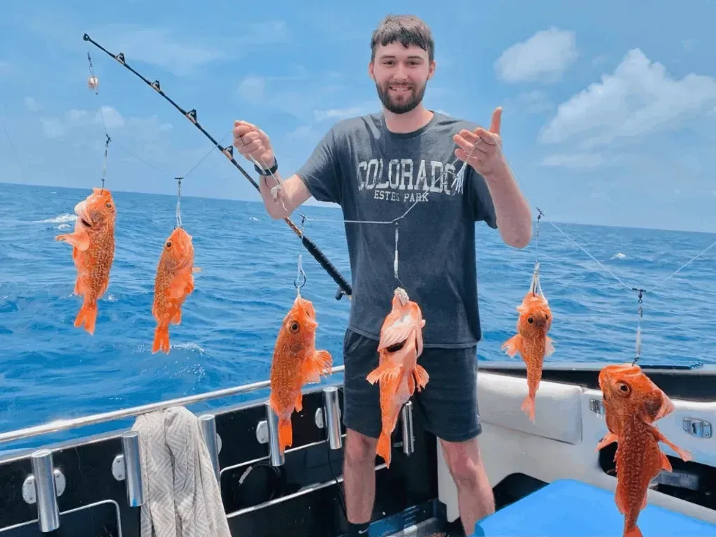 A man is standing on a boat holding a fishing rod and fish.