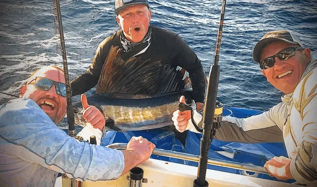 Three men are fishing on a boat and one of them is holding a large fish.