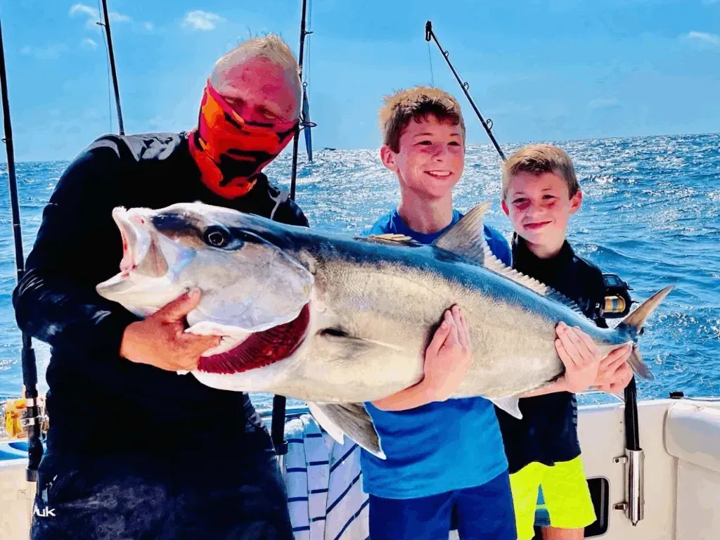 A man and two boys are holding a large fish on a boat.