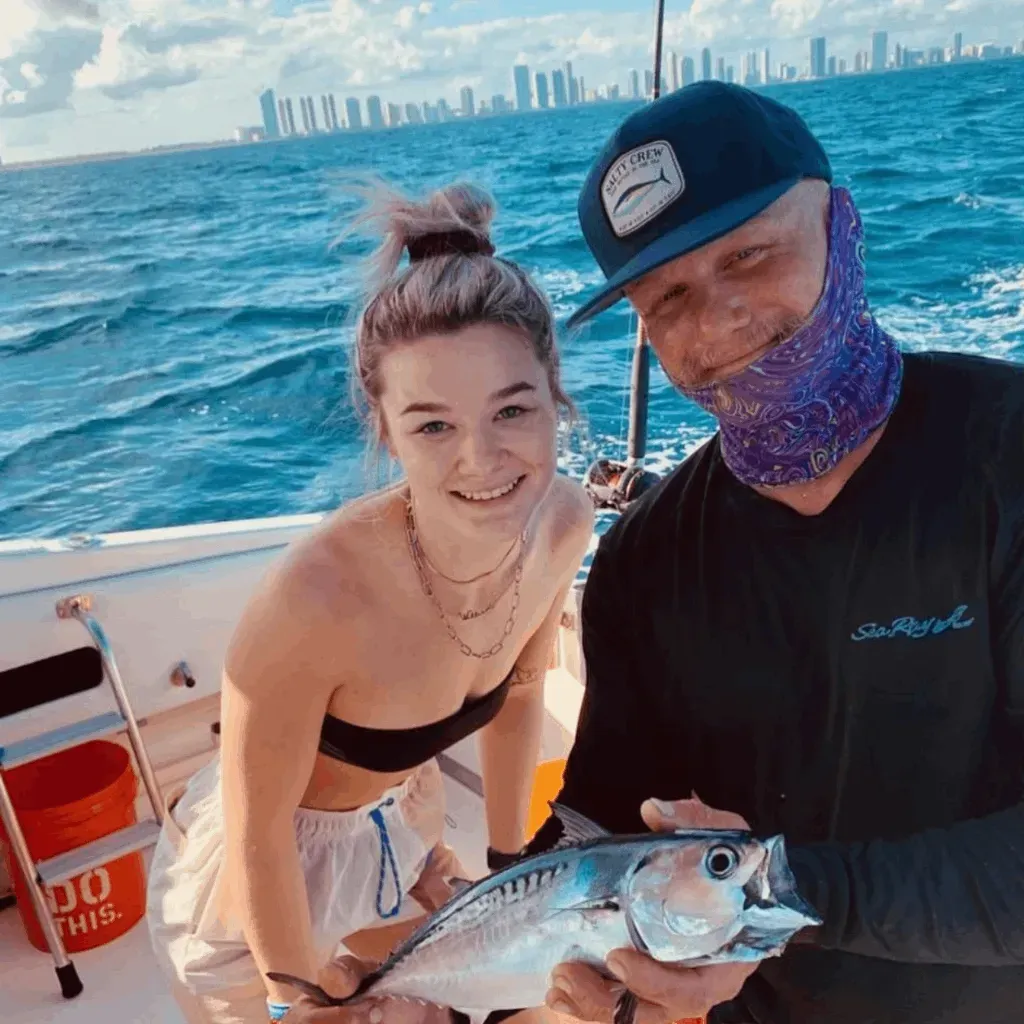 A man and a woman are standing on a boat holding a fish.