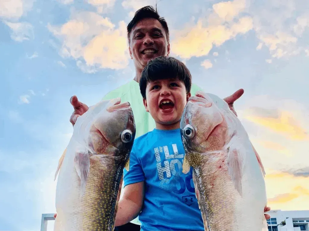 A man and a boy are holding two fish in their hands.