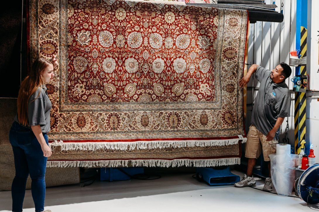 Two people unrolling a large red patterned rug in a warehouse.