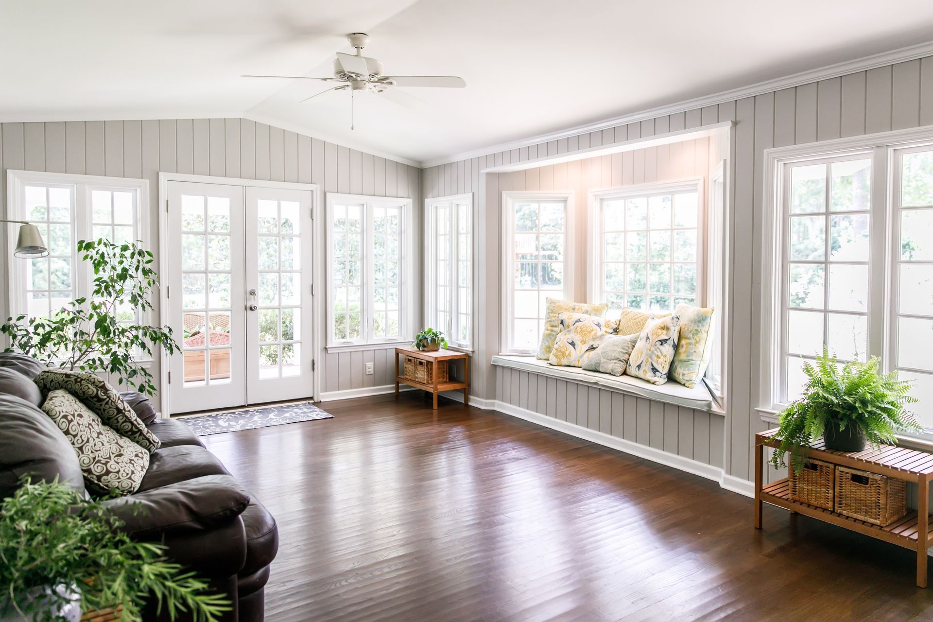 Salon avec parquet foncé, grandes fenêtres et banquette intégrée.