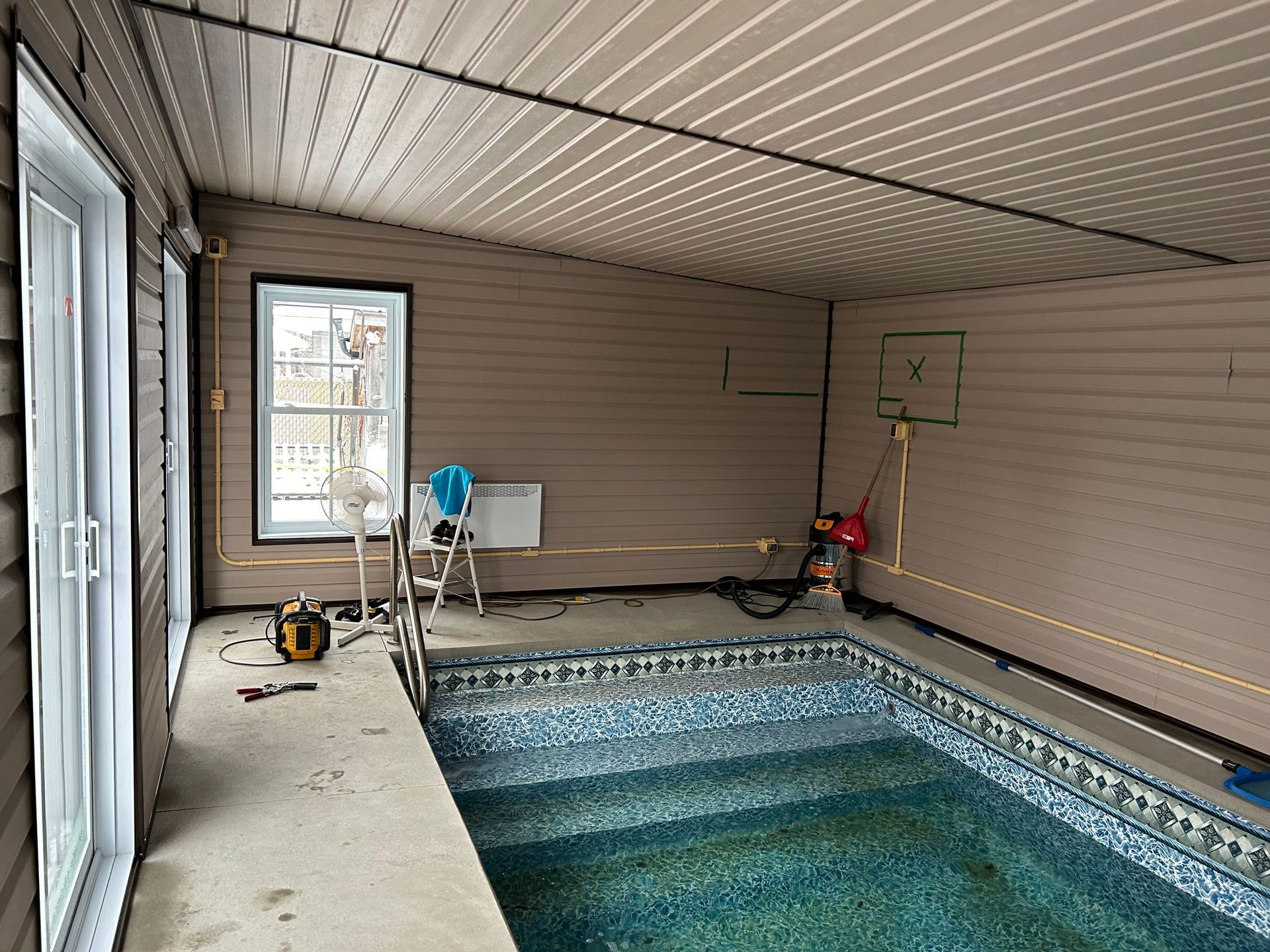 Piscine intérieure sous une terrasse couverte. Des outils et du matériel électrique sont visibles près de la piscine.