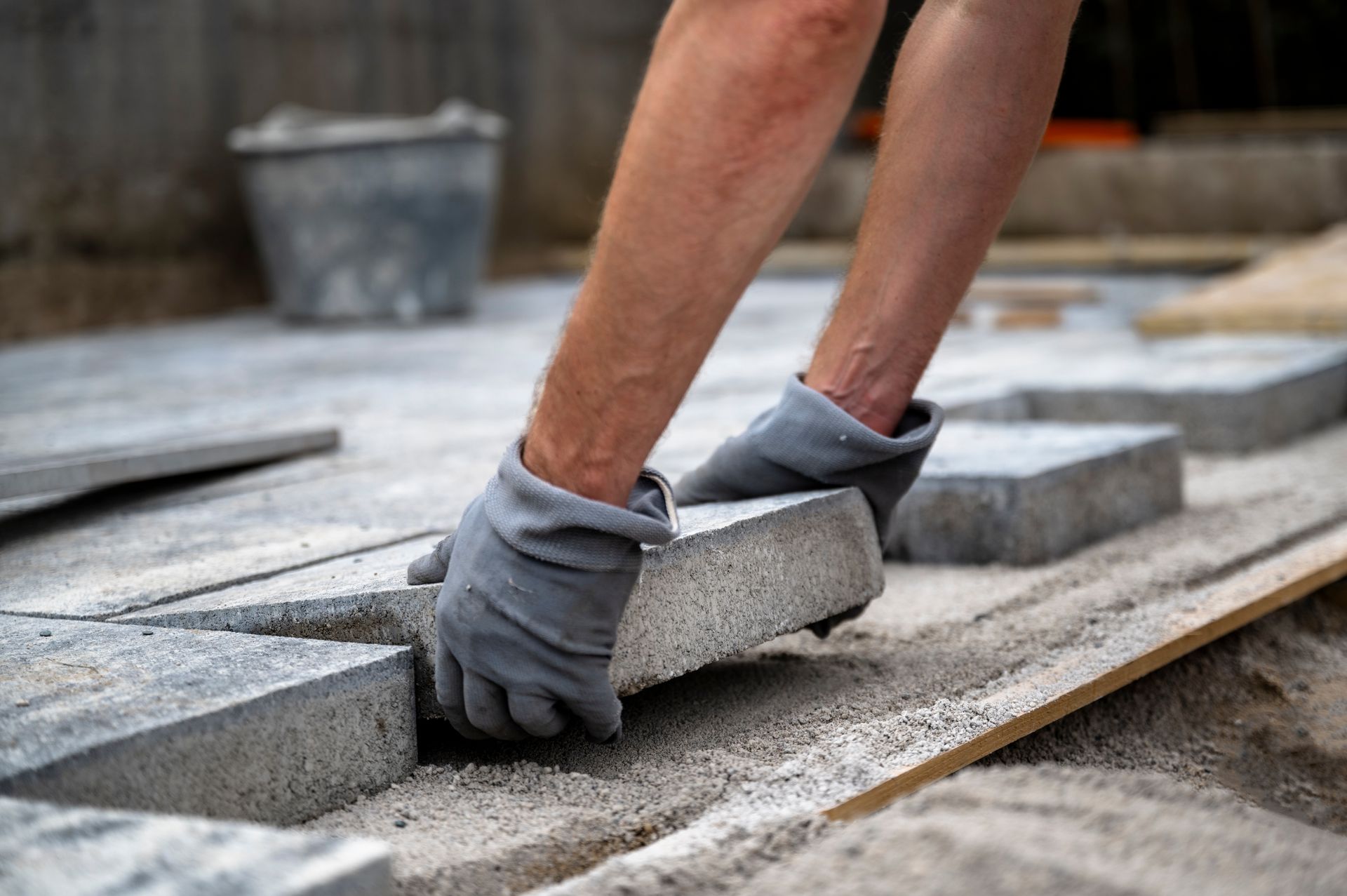 Une personne portant des gants gris pose des pavés gris sur une surface préparée.