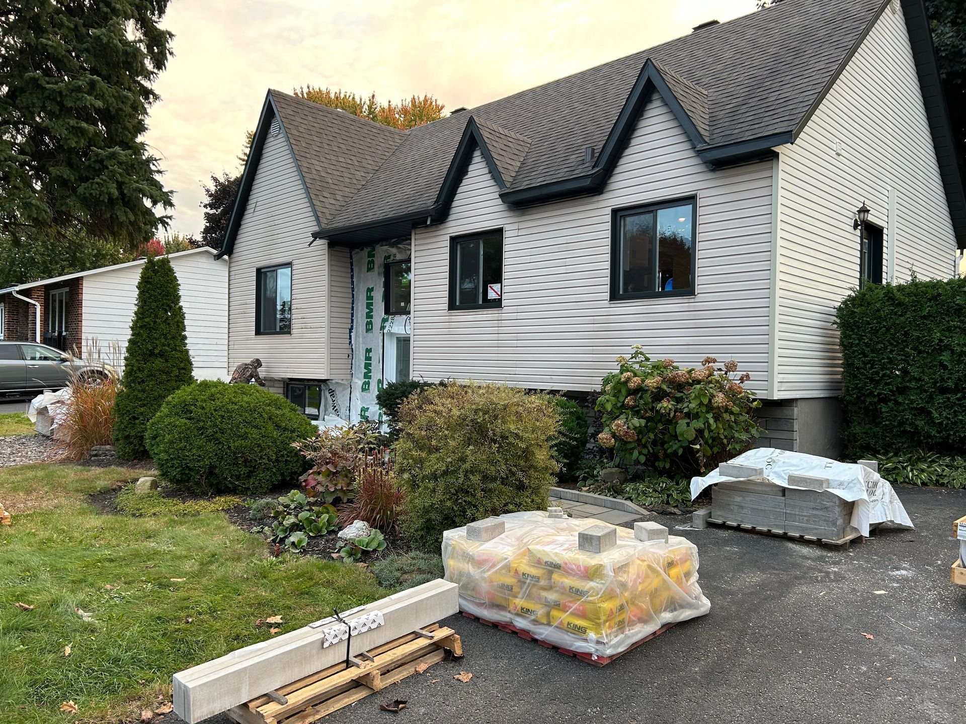 Façade de la maison en rénovation. Bardage blanc, toit foncé, matériaux de construction sur l'allée.