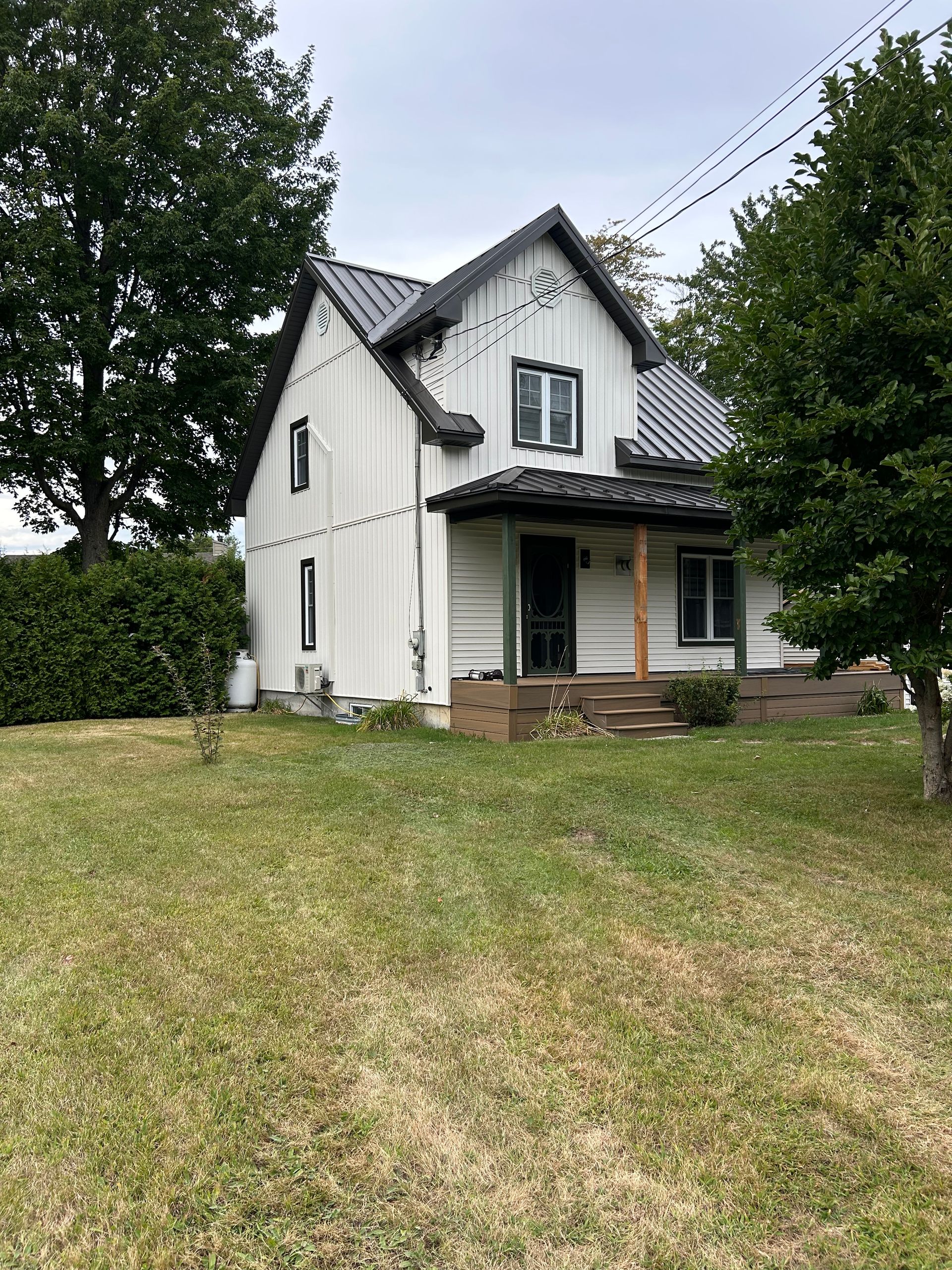 Maison blanche à deux étages avec toit et boiseries noires, petit porche et jardin gazonné par temps nuageux.