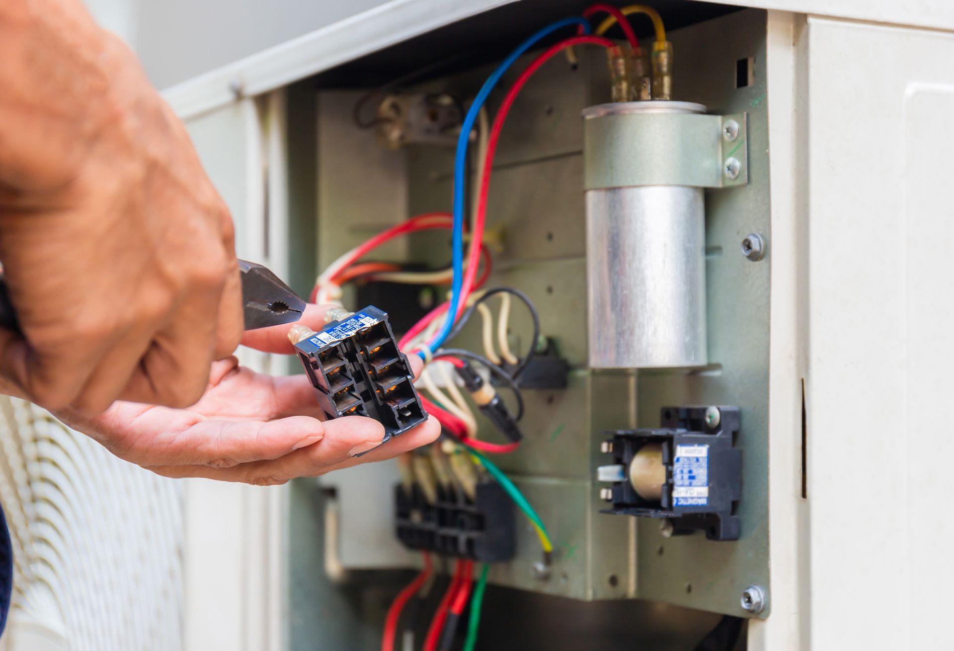 Hand holding a circuit board near an open electrical panel with red, blue, and green wires