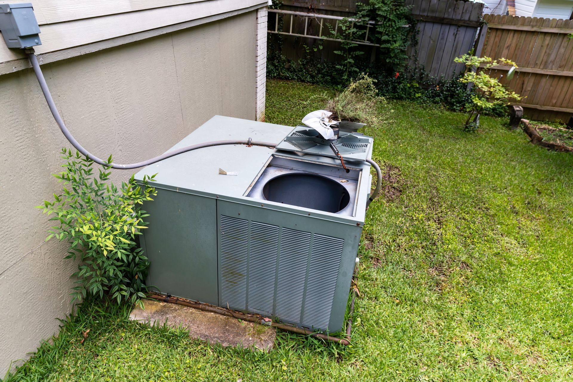 Outdoor HVAC unit beside a house, with its top cover open and grassy yard around it