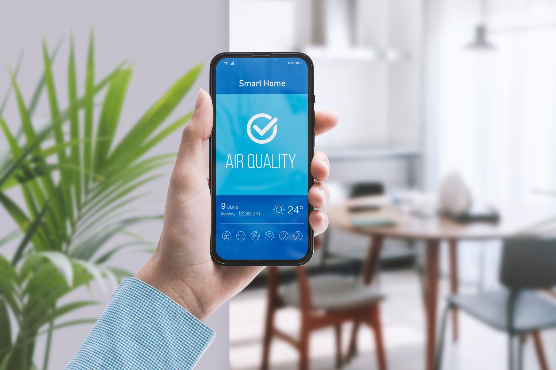Hand holding a smartphone showing a blue “Quality” app screen in a bright office setting