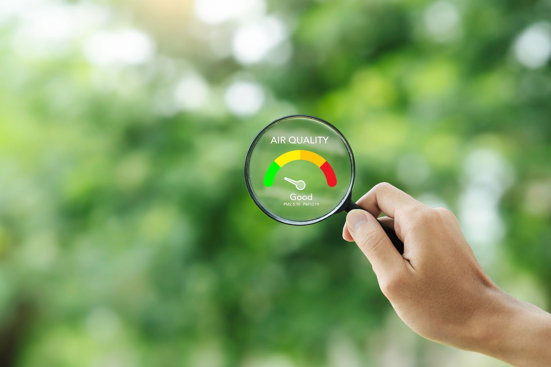 Hand holding magnifying glass over green environmental gauge on blurred green background