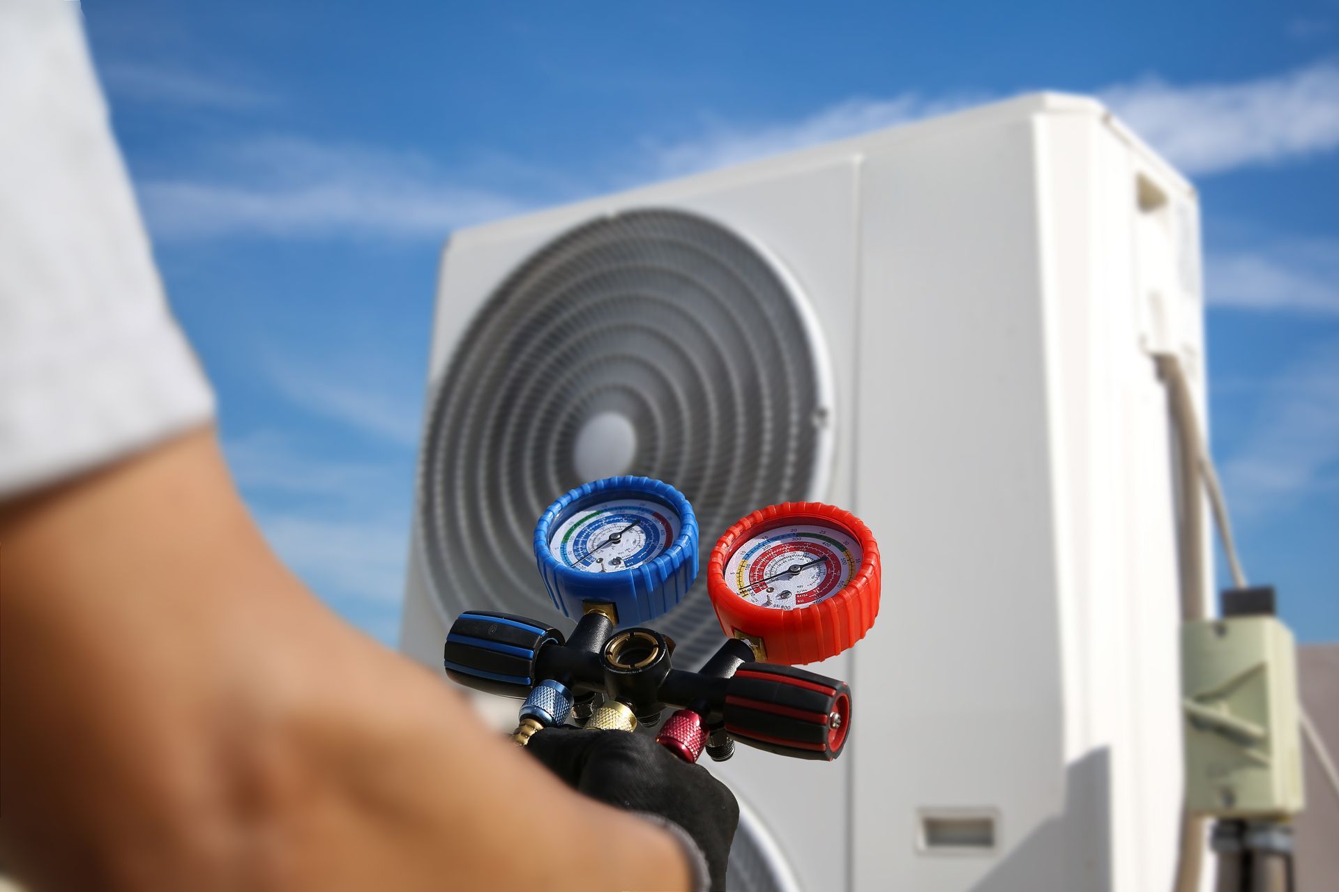 Technician holding manifold gauges near an outdoor air conditioner unit