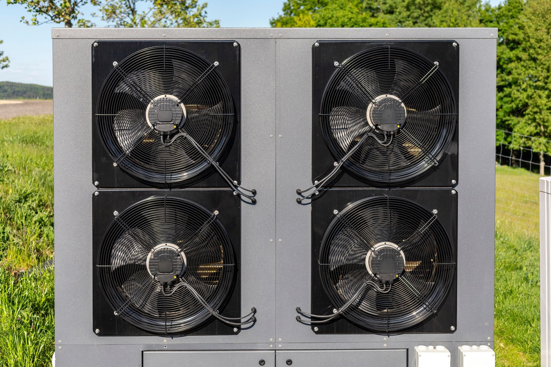 Four black fans mounted on a gray metal panel outdoors in a field