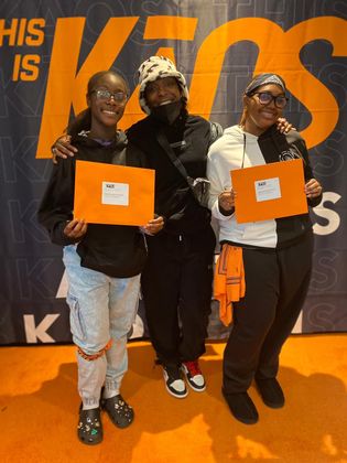 Three people smiling, holding orange envelopes. Against a backdrop with the words 