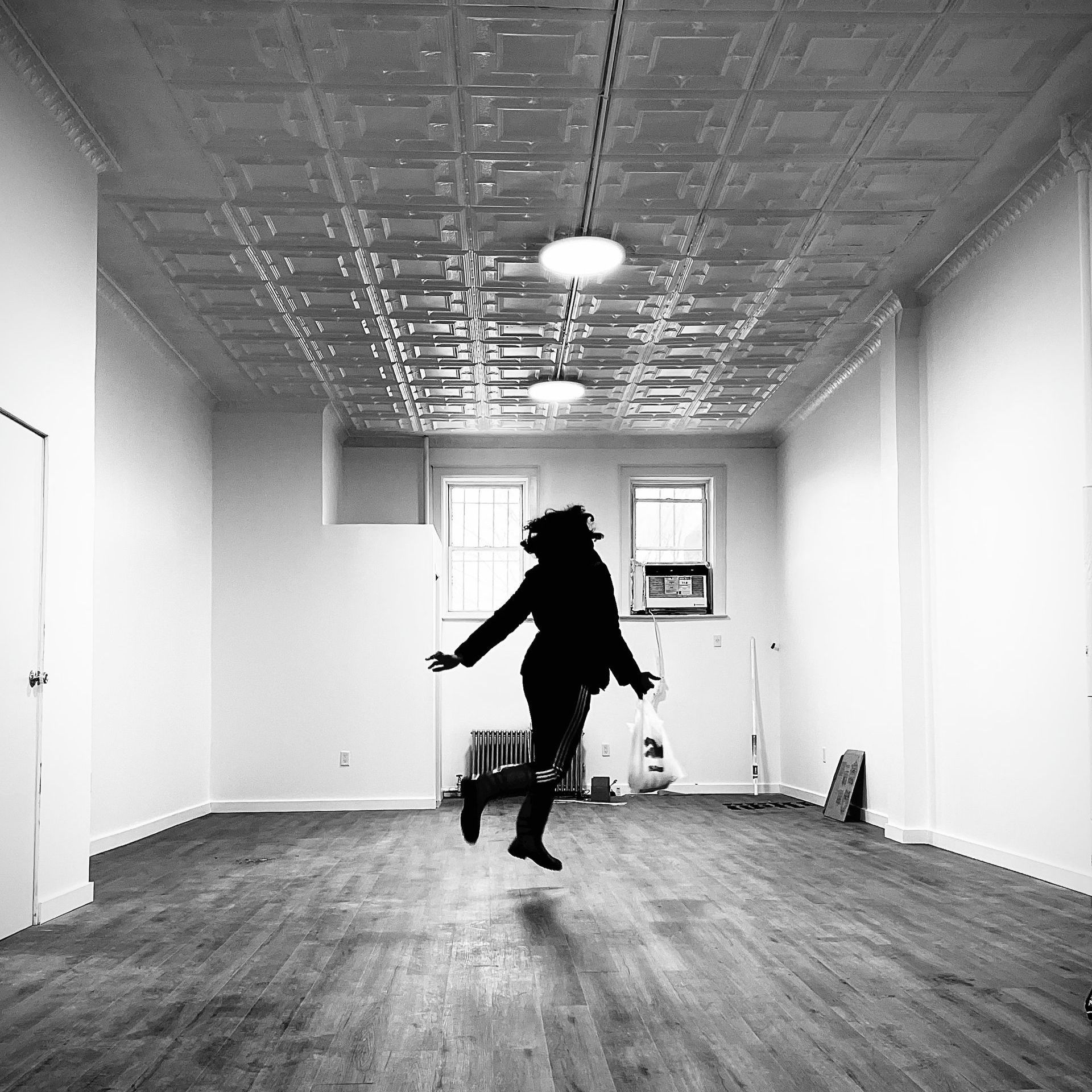 A silhouetted person jumps joyfully in an empty room with a decorative ceiling.