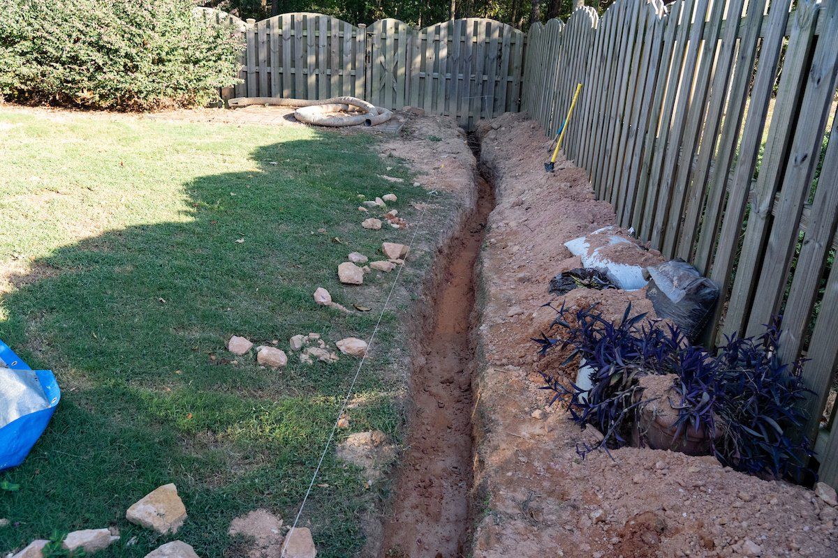 A hole in the ground in a backyard next to a wooden fence.