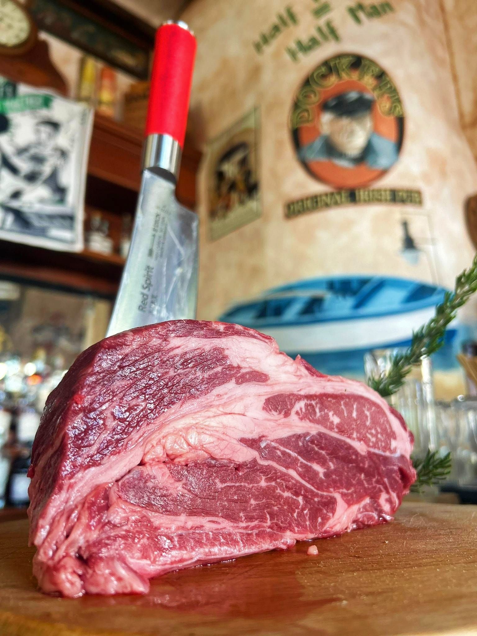 Bistecca cruda su una tavola di legno, con un coltello dal manico rosso e un murale sullo sfondo.