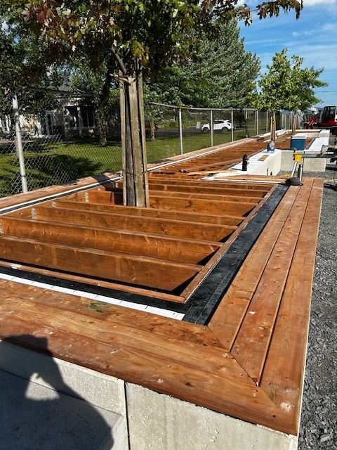 Une terrasse en bois est en cours de construction dans un parc avec un arbre en arrière-plan.