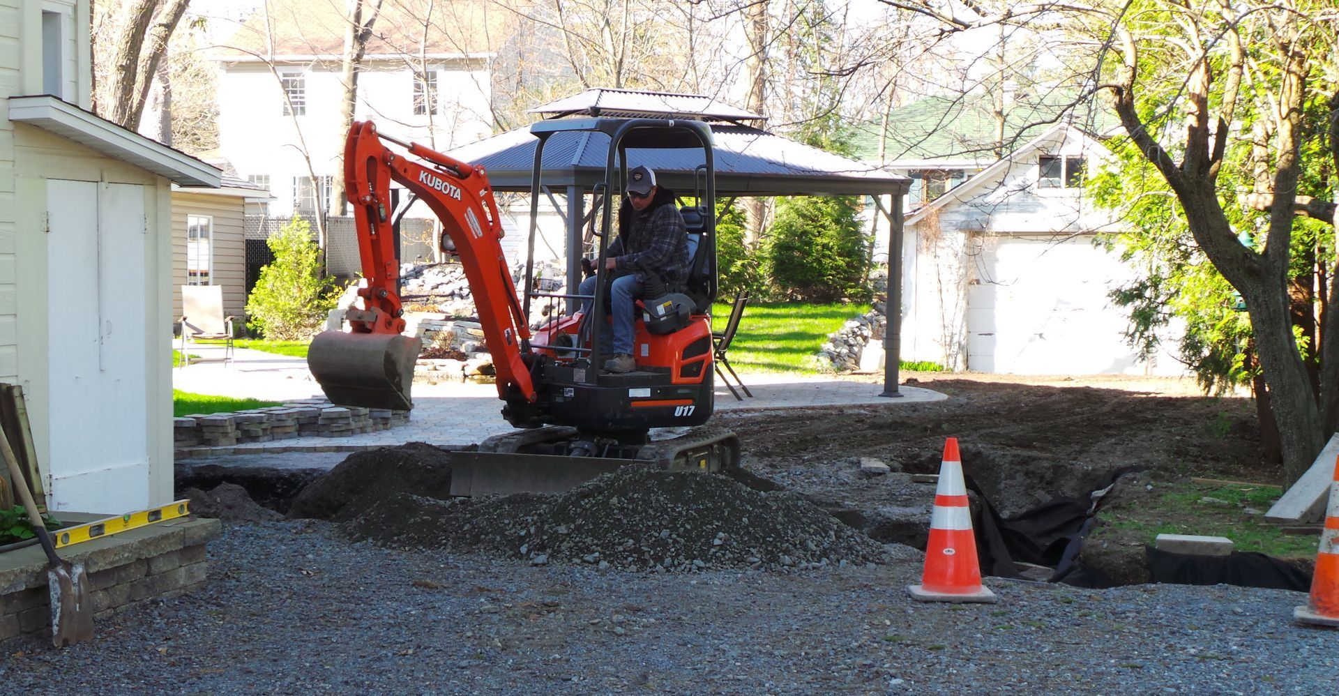 Un homme conduit une petite excavatrice rouge dans une allée