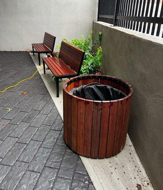 Une poubelle en bois se trouve à côté d'un banc en bois