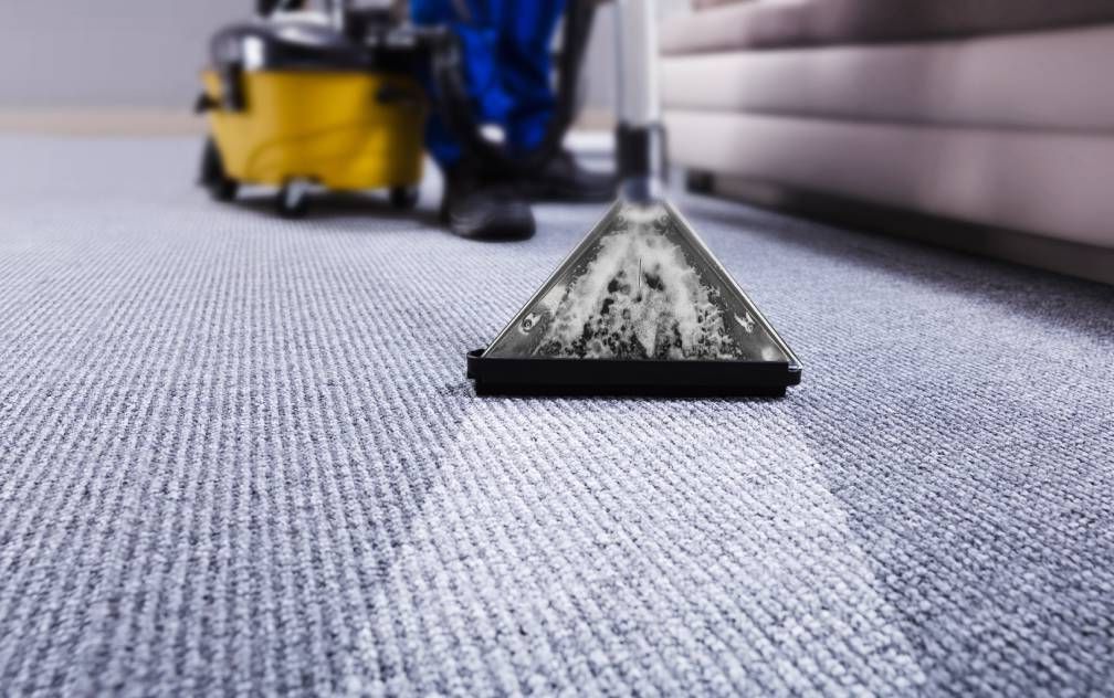 Carpet cleaner vacuuming a gray carpet with a yellow machine in the background