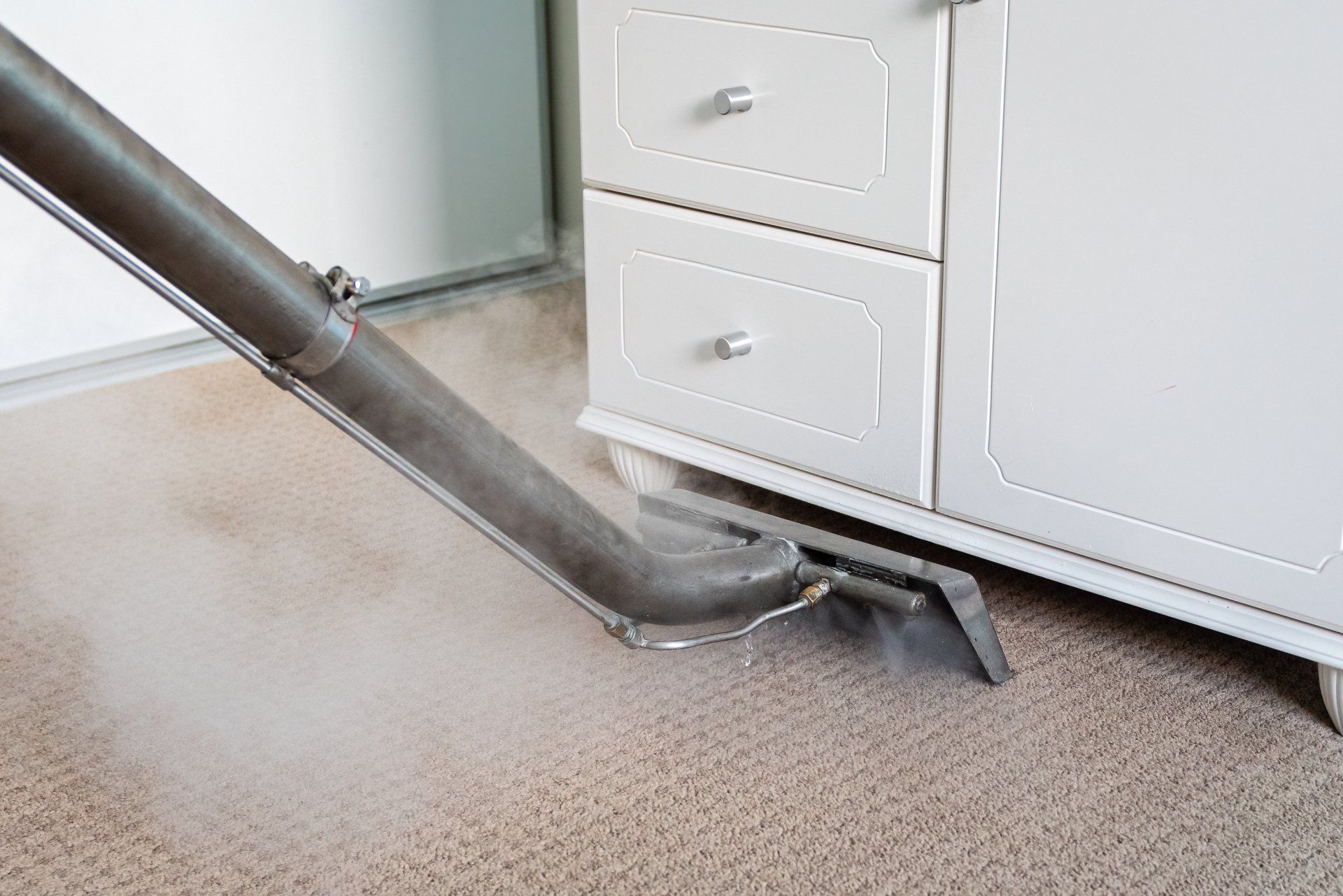Vacuum hose cleaning carpet beside white dresser and wall