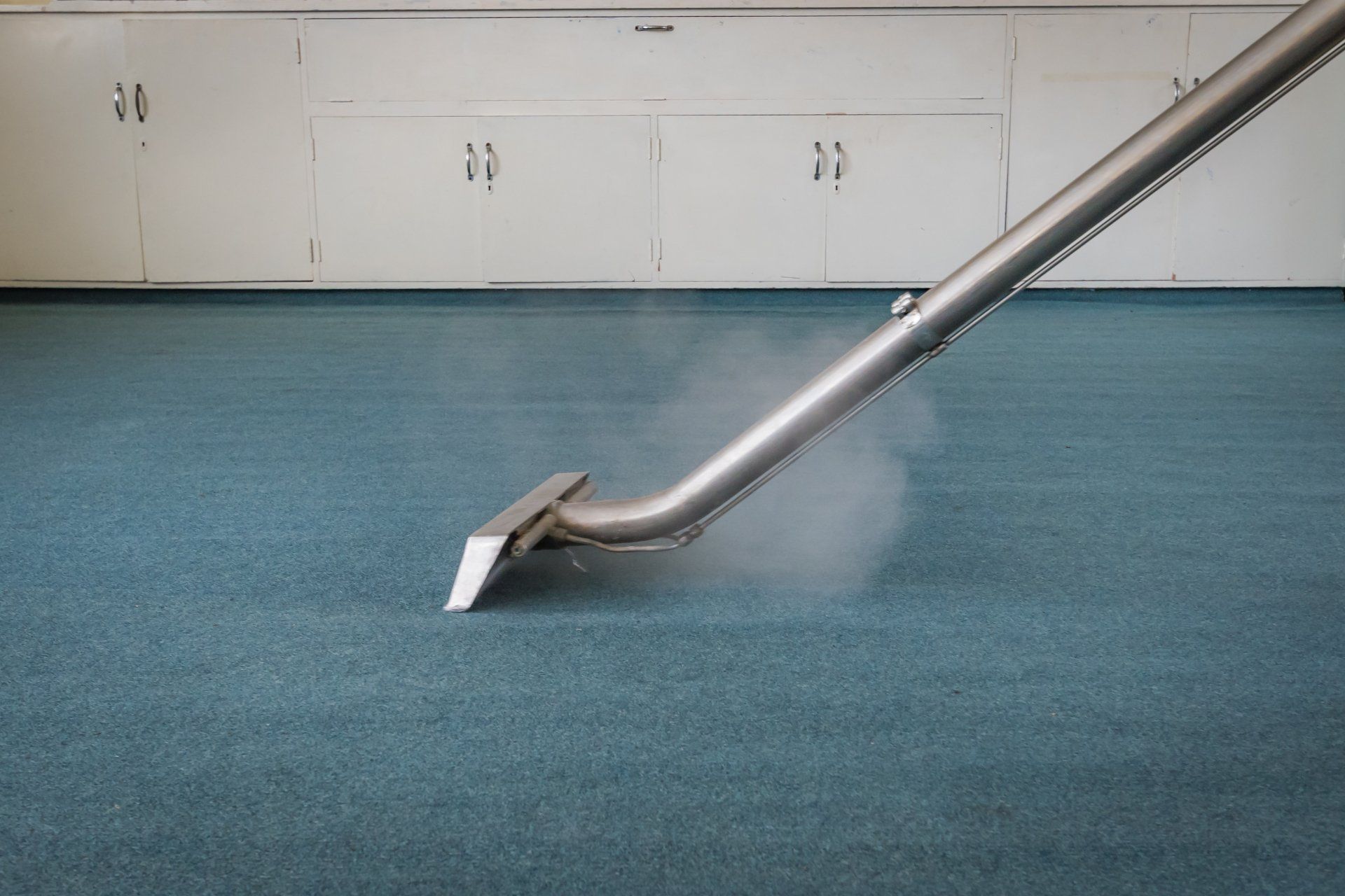 Vacuum cleaner head on blue carpet beside white wall