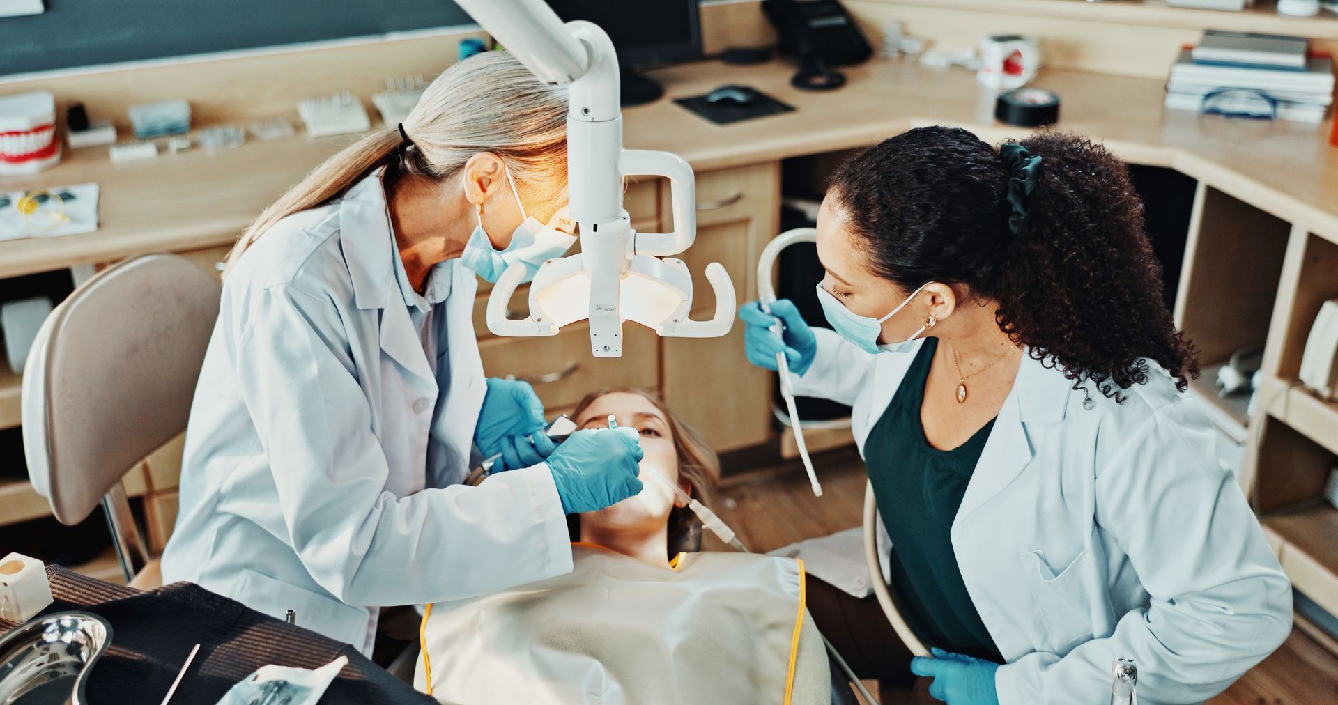 Dentist, team and patient in clinic for procedure, dental suction and drill for cleaning tooth decay