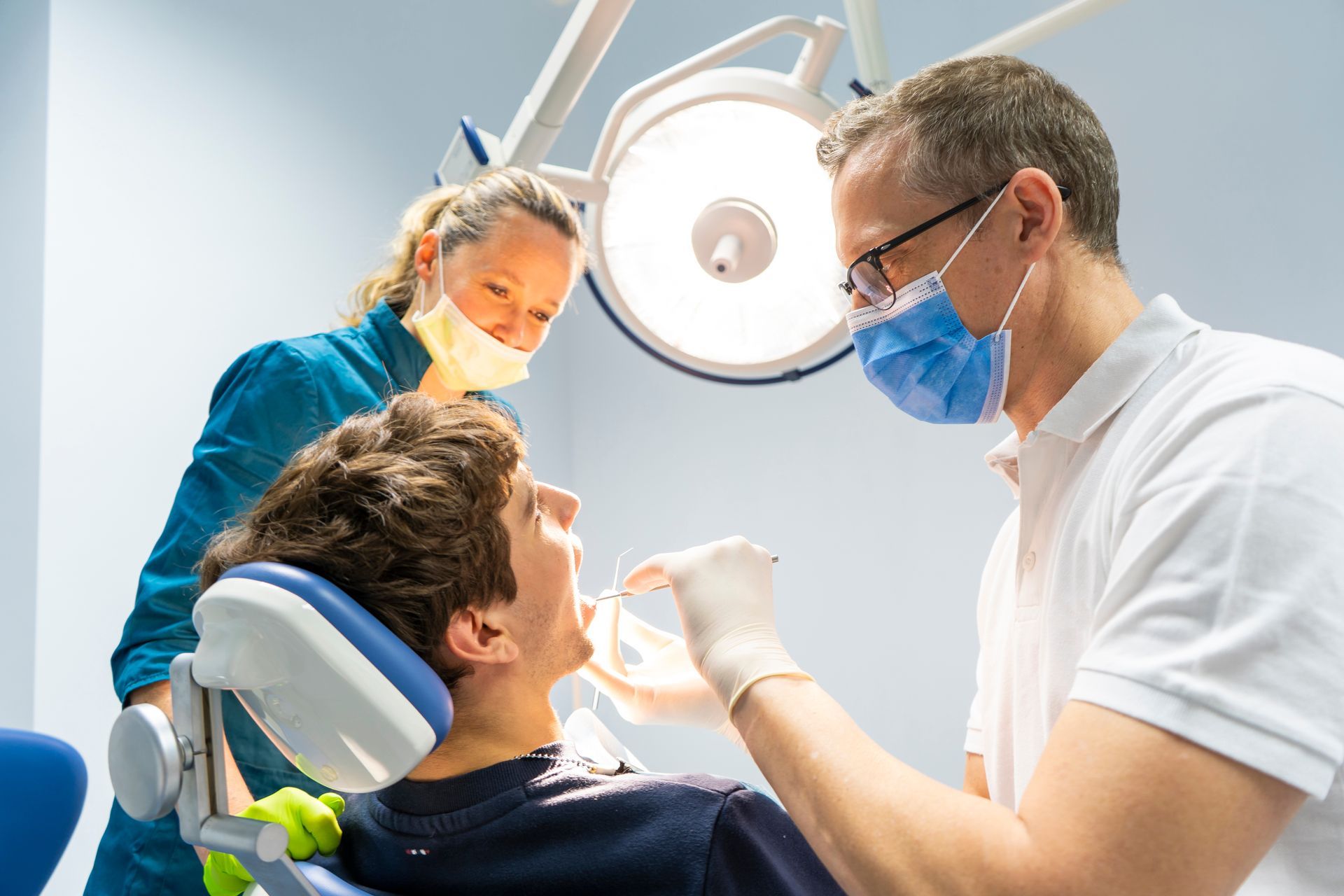 Dentist treating a patient in a clinic, with assistant and overhead exam light