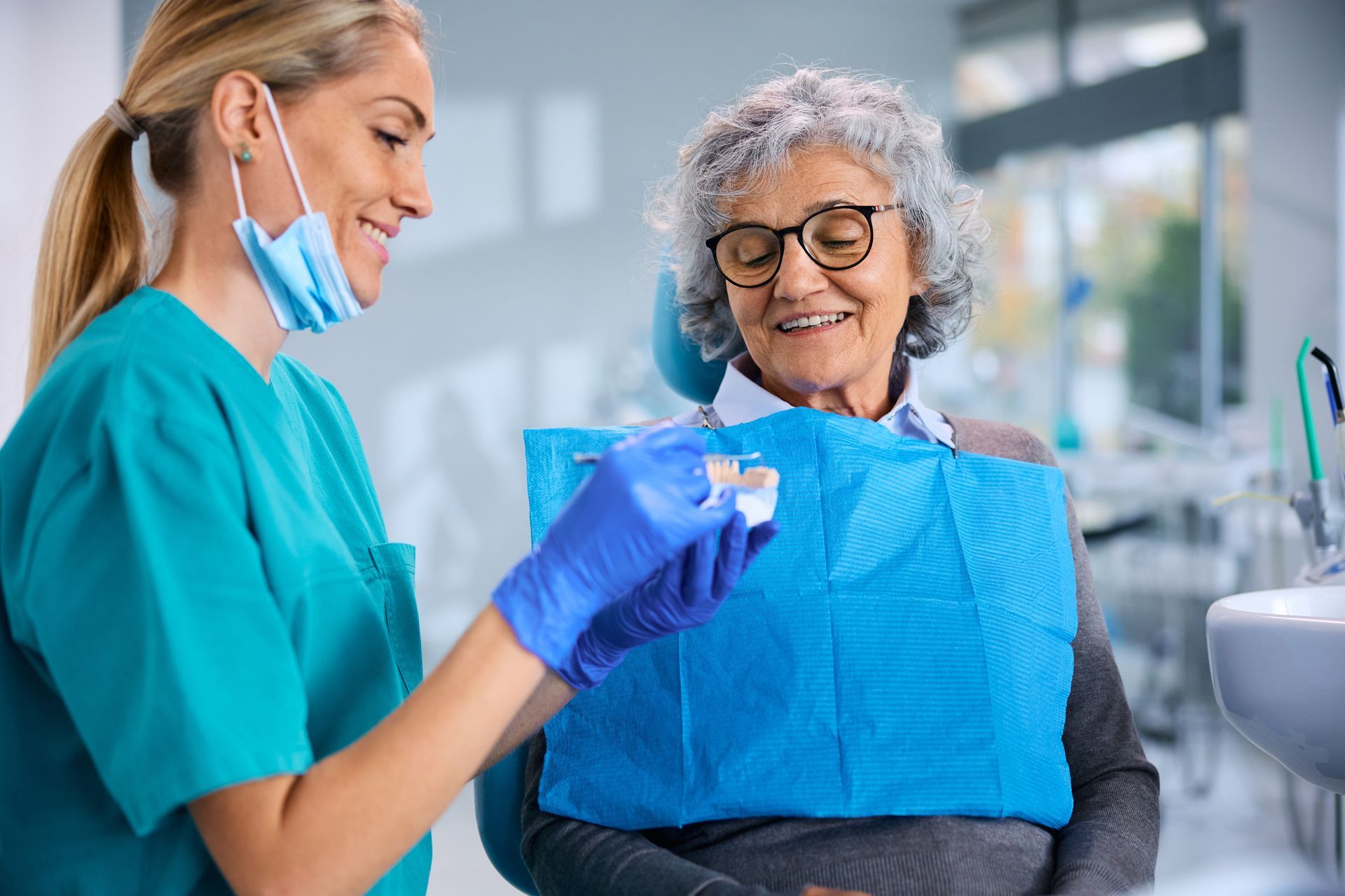 Dentist handing a blue dental bib to a smiling patient in a bright clinic