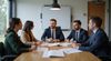 Five people in business attire sit around a conference table, engaged in a discussion.