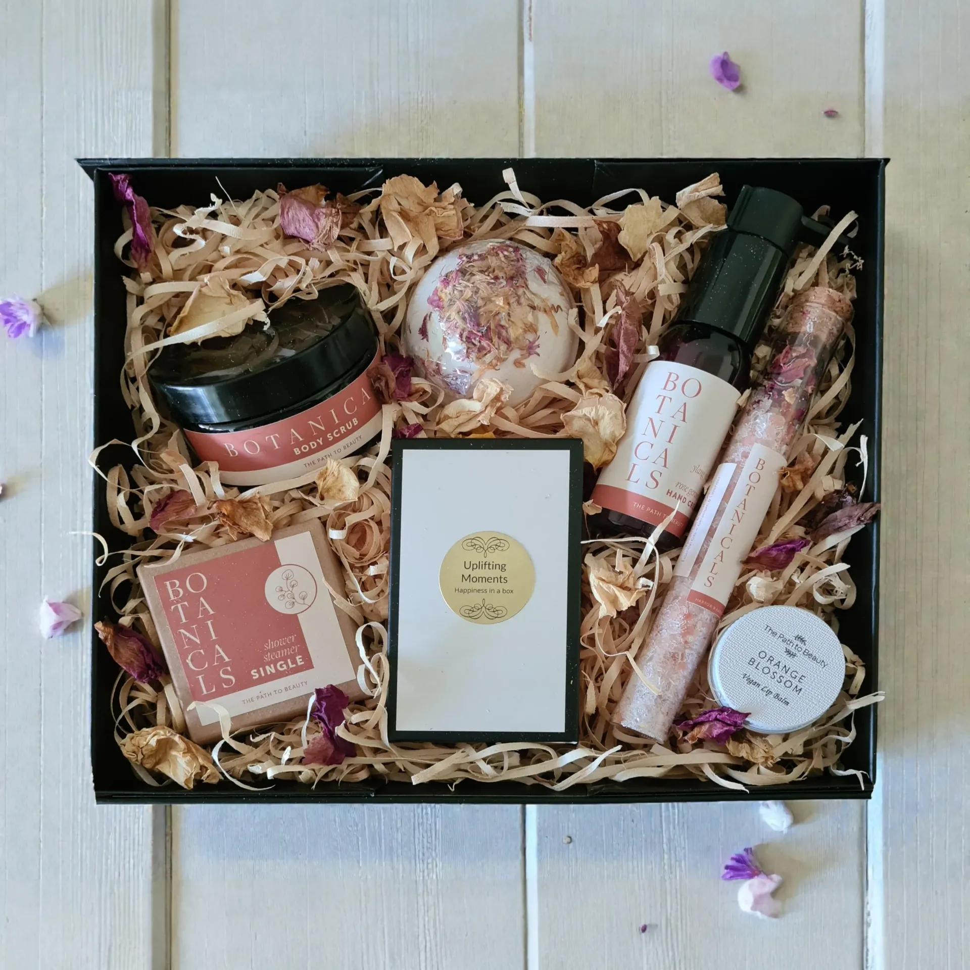 Assorted pink and beige beauty products arranged in a gift box with shredded paper filler.