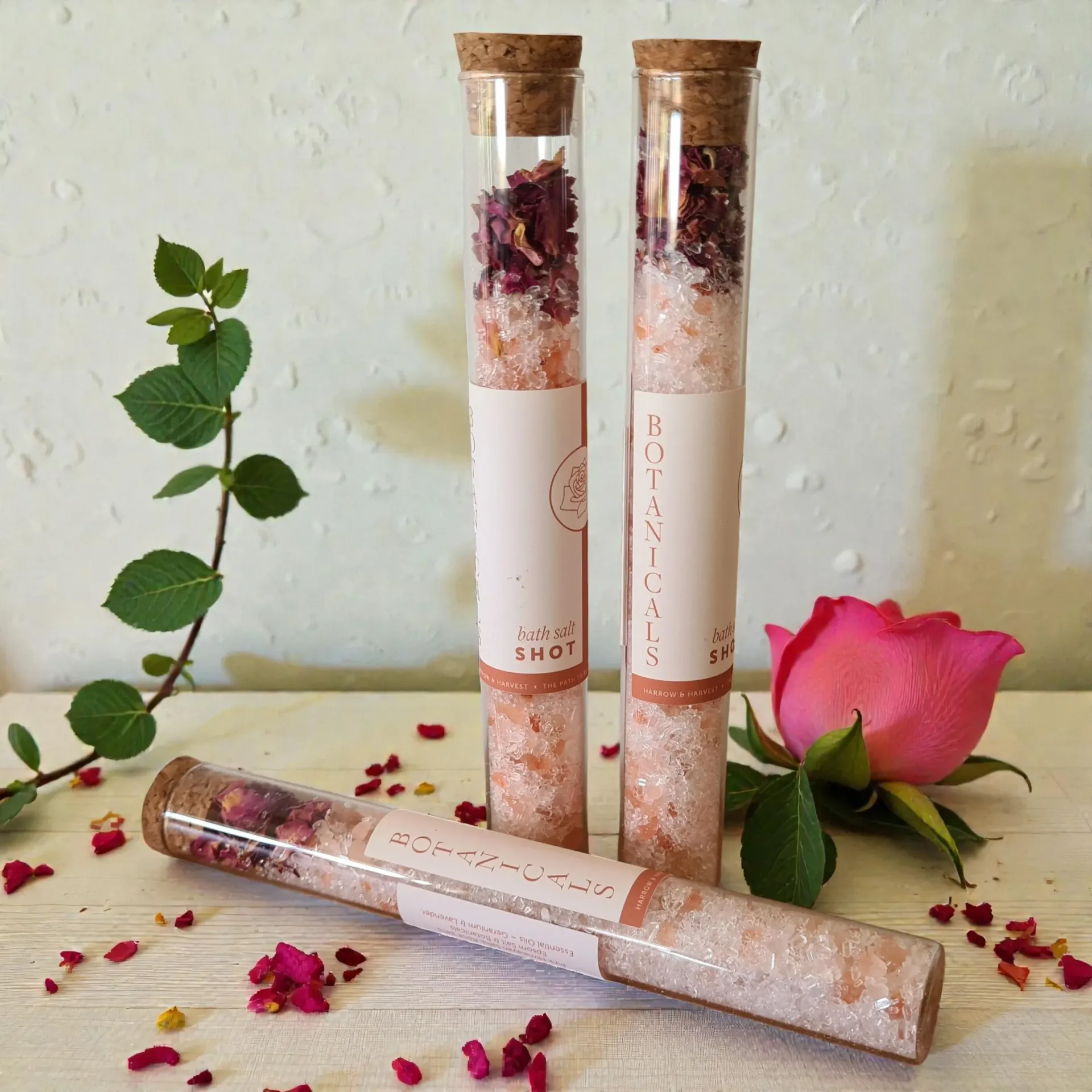 Rose-scented cosmetic tubes with dried petals and a pink rose on a white tabletop
