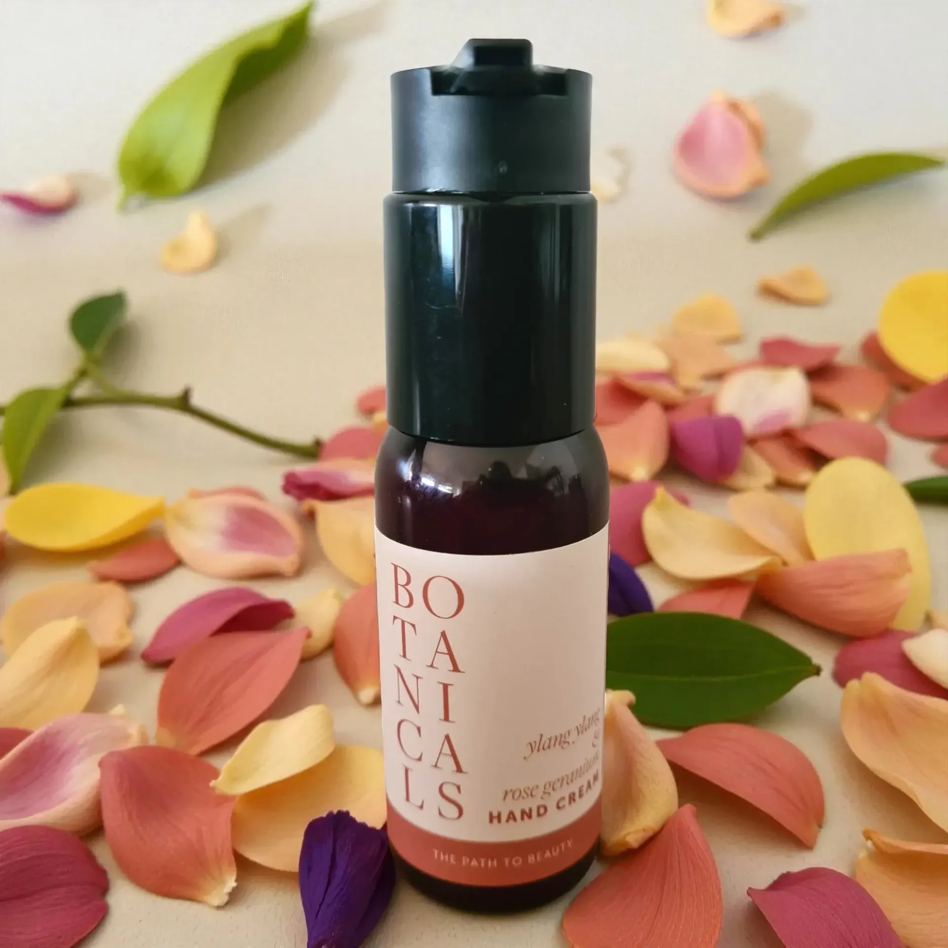 Dark bottle of hand cream with pink label, surrounded by scattered pastel flower petals.