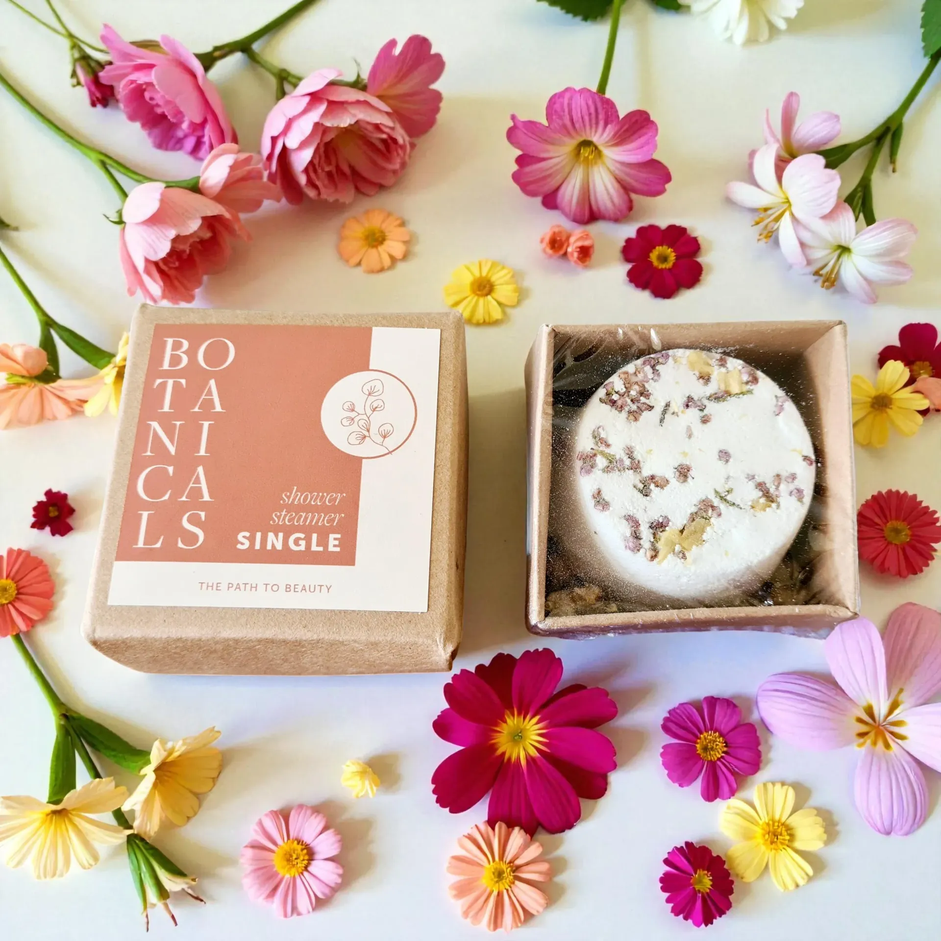 Botanicals gift box with a shower steamer, surrounded by pink and yellow flowers on a white background